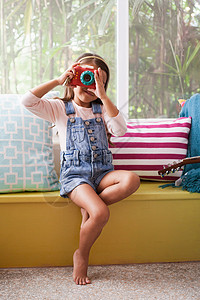 窗口沙发上用玩具照相机拍摄的女孩图片