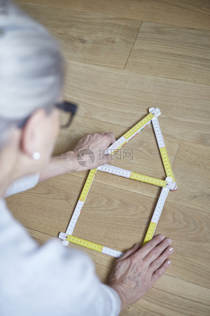 地板上装有房屋成型胶带测量器的妇女图片