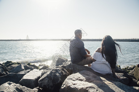 成年中期坐在海边岩石上看风景的一对夫妻背景