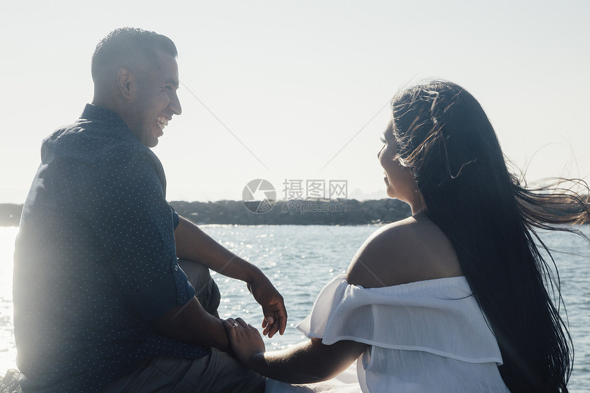 坐在沿海岩石上手牵手笑着的情侣图片
