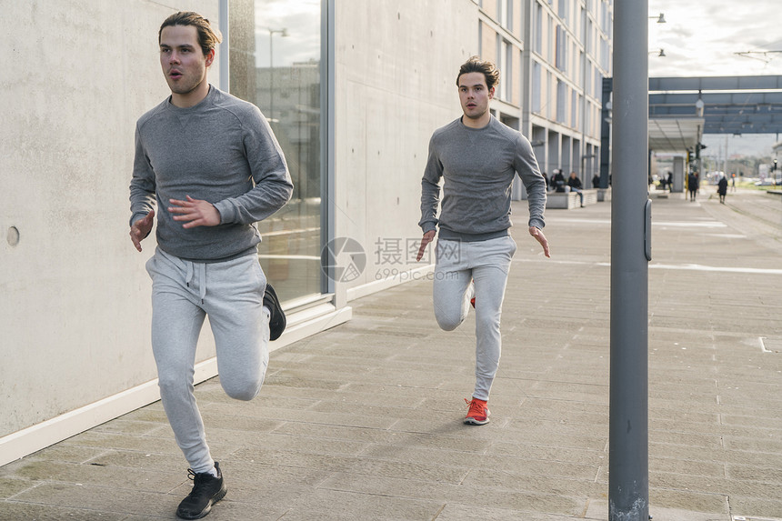 年轻男双胞胎对沿城市人行道跑步图片