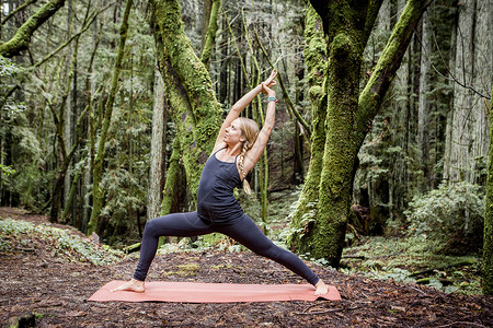 瑜伽树式在森林里做武士瑜伽的年轻女子背景