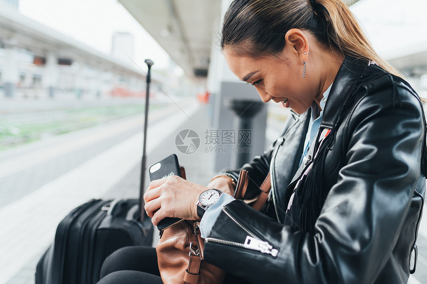 坐在火车平台上的女人拿着手机翻手提包图片