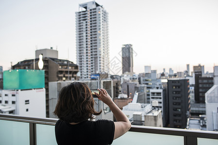 从日本大阪阳台拍摄日落照片的妇女图片