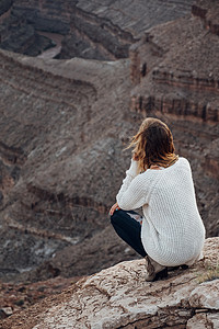 美国犹他州一名年轻女子蹲在岩石上看着风景高清图片