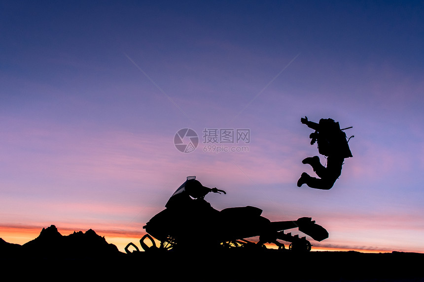 日落时分加拿大不列颠哥伦比亚省惠斯勒市停着的摩托车旁一个人欢蹦乱跳的剪影图片