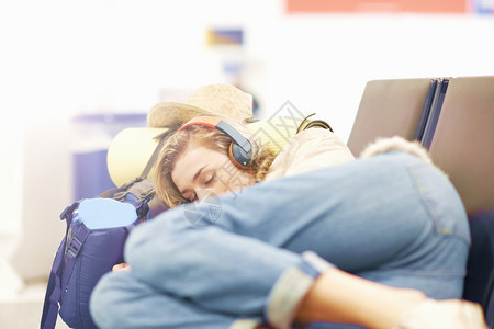 在机场的年轻妇女睡在出发休息室的座位上图片