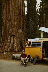 在公园树下休息的开野营面包车的成年男子图片