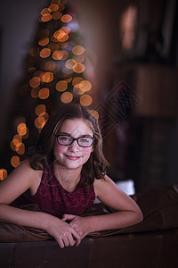 在圣诞树背景下女孩靠在沙发上微笑图片