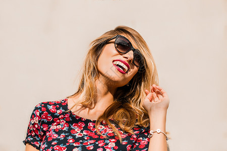 女人戴着太阳眼镜在墙前摸着头发笑图片