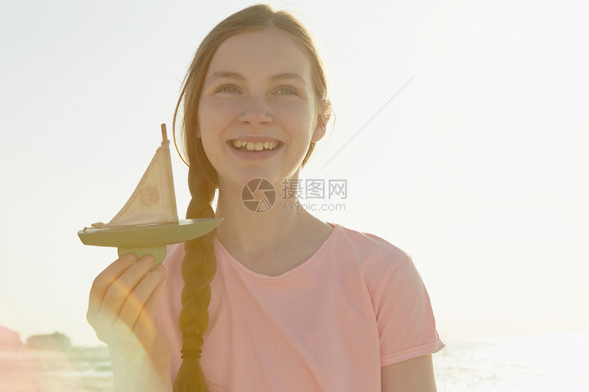 女孩在海边拿着玩具船微笑图片