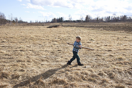 男孩抱着木杆走过田地高清图片