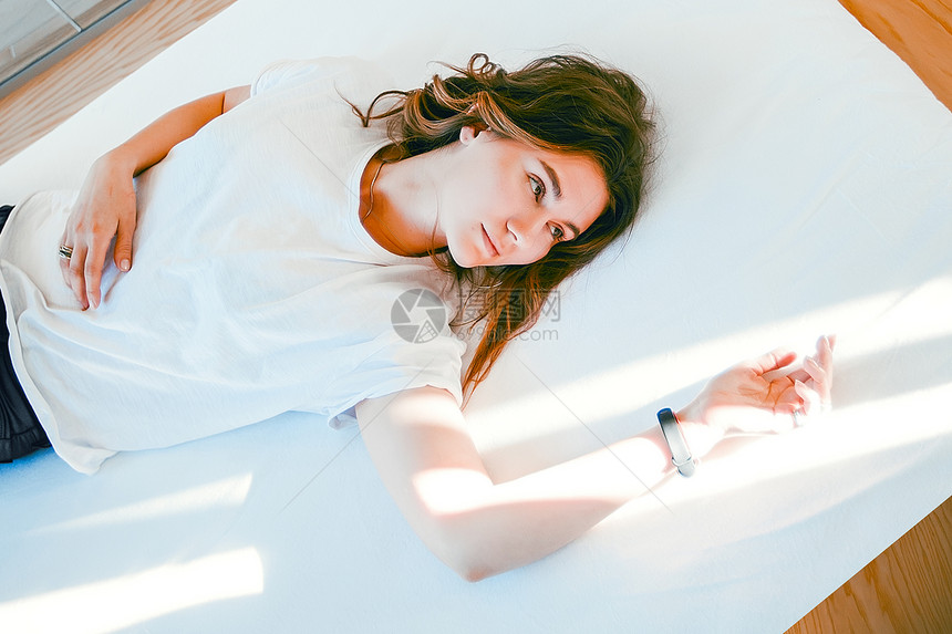 年轻女士在床上放松手臂在光线下休息深思熟虑的表情图片