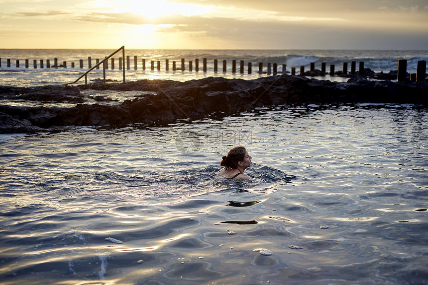 西班牙加那利群岛大加那利岛拉斯帕尔马斯日落时在海滨游泳池游泳的妇女图片
