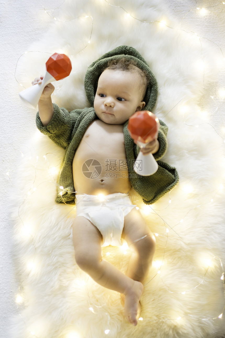 婴儿男孩躺在毛地毯上装饰着灯光的中与响声玩耍图片