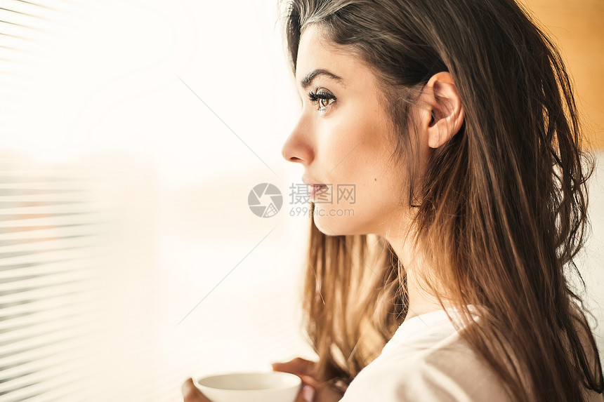女人端着杯子在窗边思考图片