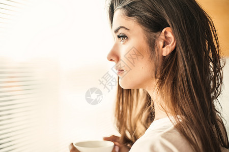 女人端着杯子在窗边思考图片