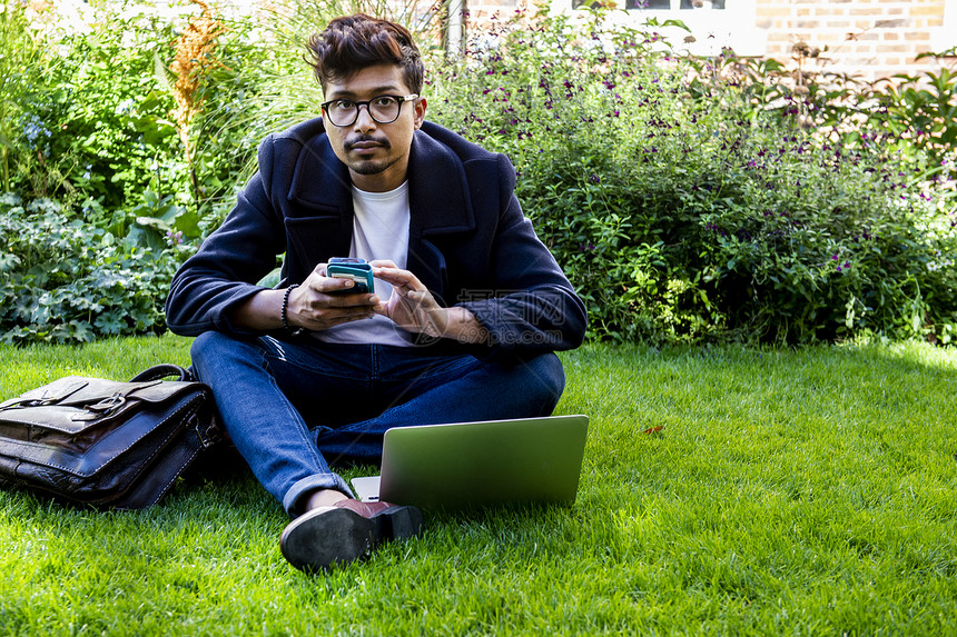 坐在草地上用手机和笔记本电脑的商人图片