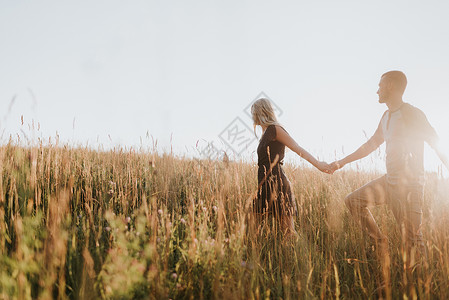 浪漫的男人和女友在阳光长草田里握着手行走图片