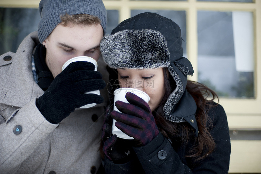 戴冬帽的年轻夫妇喝着外送咖啡图片