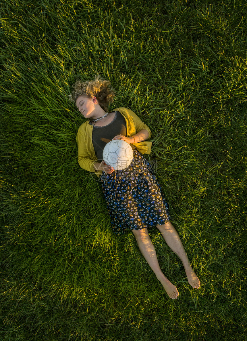 年轻女孩躺在草地上眼睛闭着眼睛拿足球俯视图片