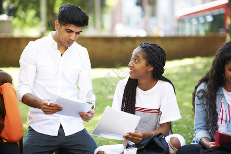 男女高等教育学生在大校园草坪上讨论文书工作图片