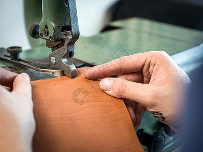 皮革工人在车间用机械加工皮袋边图片