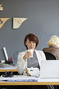 在办公桌看笔记本电脑和喝咖啡的女设计师图片