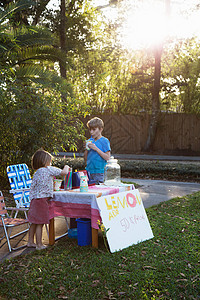 才智男孩和妹妹在花园的柠檬水摊位前站着喝水背景
