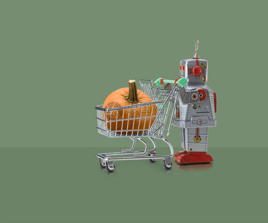 玩具机器人在绿色背景下推着装南瓜的小型购物车图片