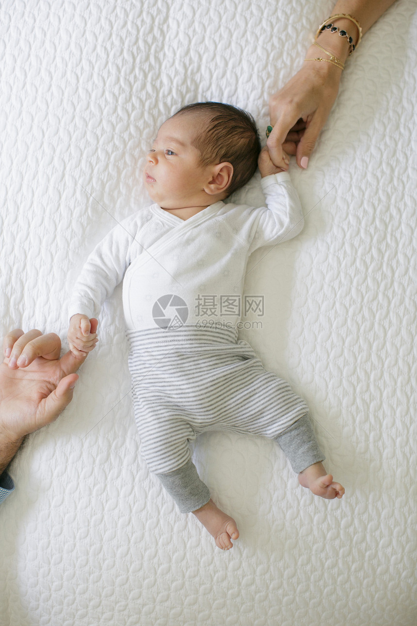 躺在床上的男婴儿牵着父母的手图片