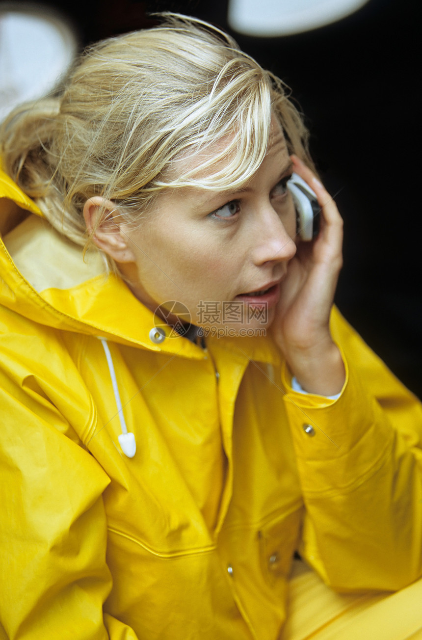 使用移动电话穿黄色雨衣的妇女图片