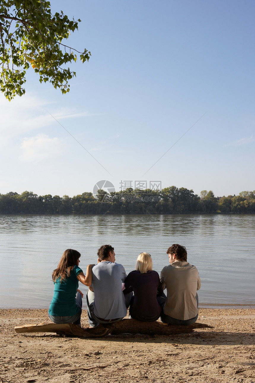 四个朋友坐在湖边的原木上图片