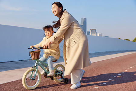 骑车游玩的女孩妈妈引导女儿骑自行车背景