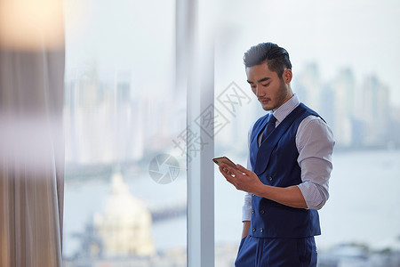 成熟商务人士站在窗前低头看手机背景