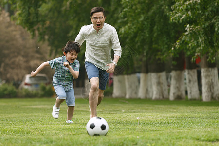 小孩树快乐父子在草地上踢足球背景