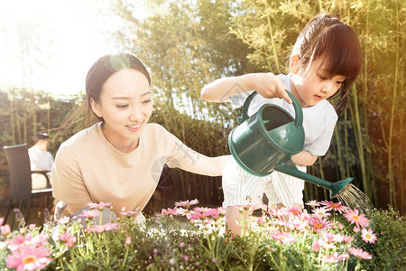 浇花的女孩年轻的母亲和女儿在浇花背景