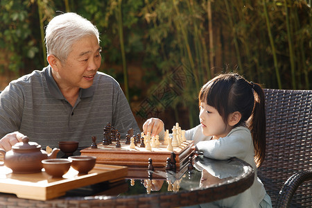 微笑无忧无虑亚洲人祖父和孙女在庭院里下棋图片