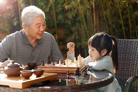 院子下棋智慧休闲60多岁祖父和孙女在庭院里下棋背景