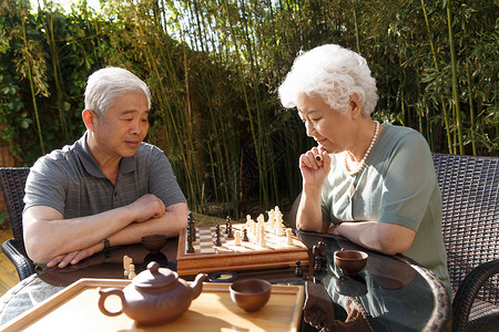 爱思考无忧无虑棋盘游戏华贵老年夫妇在院子里下棋背景