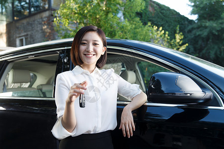 汽车销售主管青年女人拿着车钥匙站在汽车旁边背景