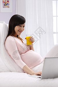 数码科技身体关注玻璃杯孕妇坐在床上看电脑高清图片