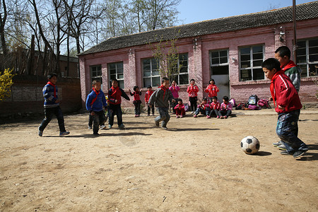 欢乐球乡村小学生在学校里踢足球背景