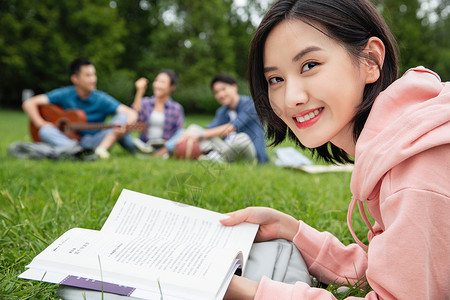 抱书的人大学生在草地上享受课余时间背景
