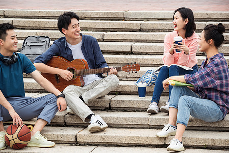抱书的女人年轻的大学生坐在台阶上弹吉他背景