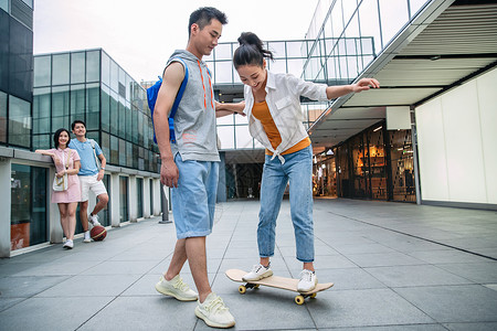 青年人帅气的大学生教女朋友滑滑板背景图片