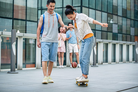 高兴的表现积极运动装帅气的大学生教女朋友滑滑板背景图片