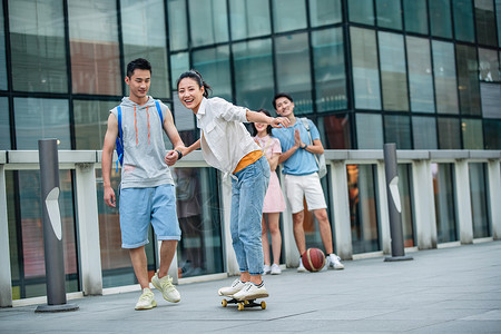 大学生篮球休闲装帅气的大学生教女朋友滑滑板背景