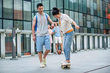 户外害怕的交流帅气的大学生教女朋友滑滑板背景图片