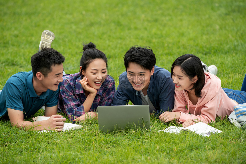 四个人享乐课余时间快乐的大学生趴在草地上学习图片